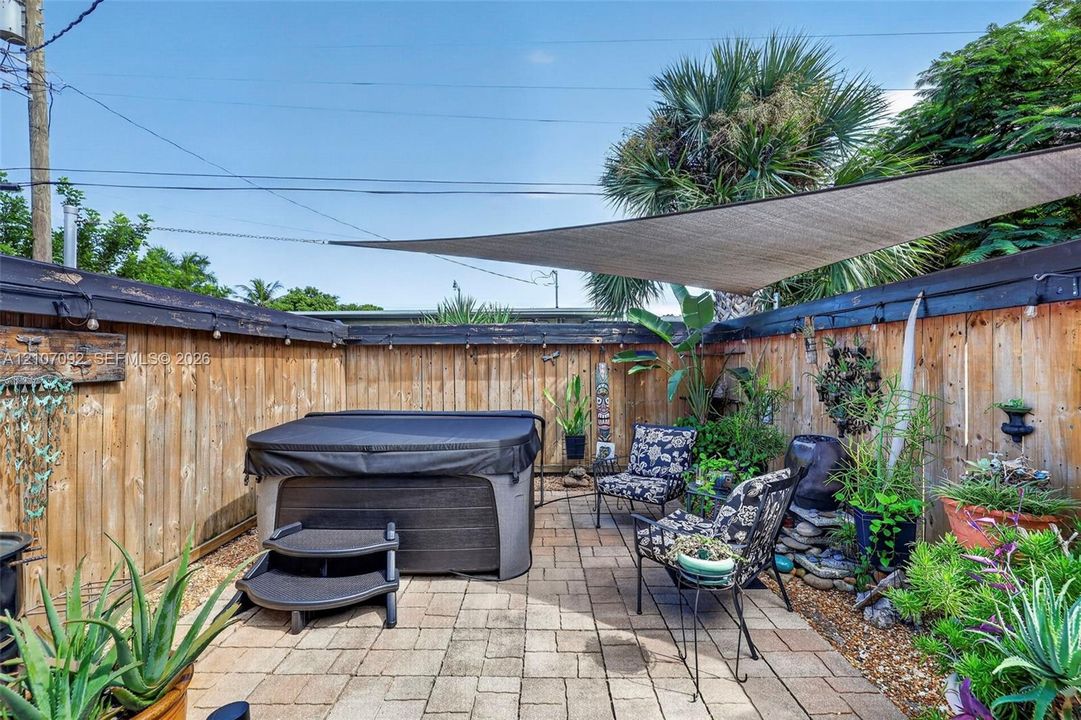 Private outdoor space featuring a paved patio, high wood-plank fencing, built-in hot tub, and overhead shade sail