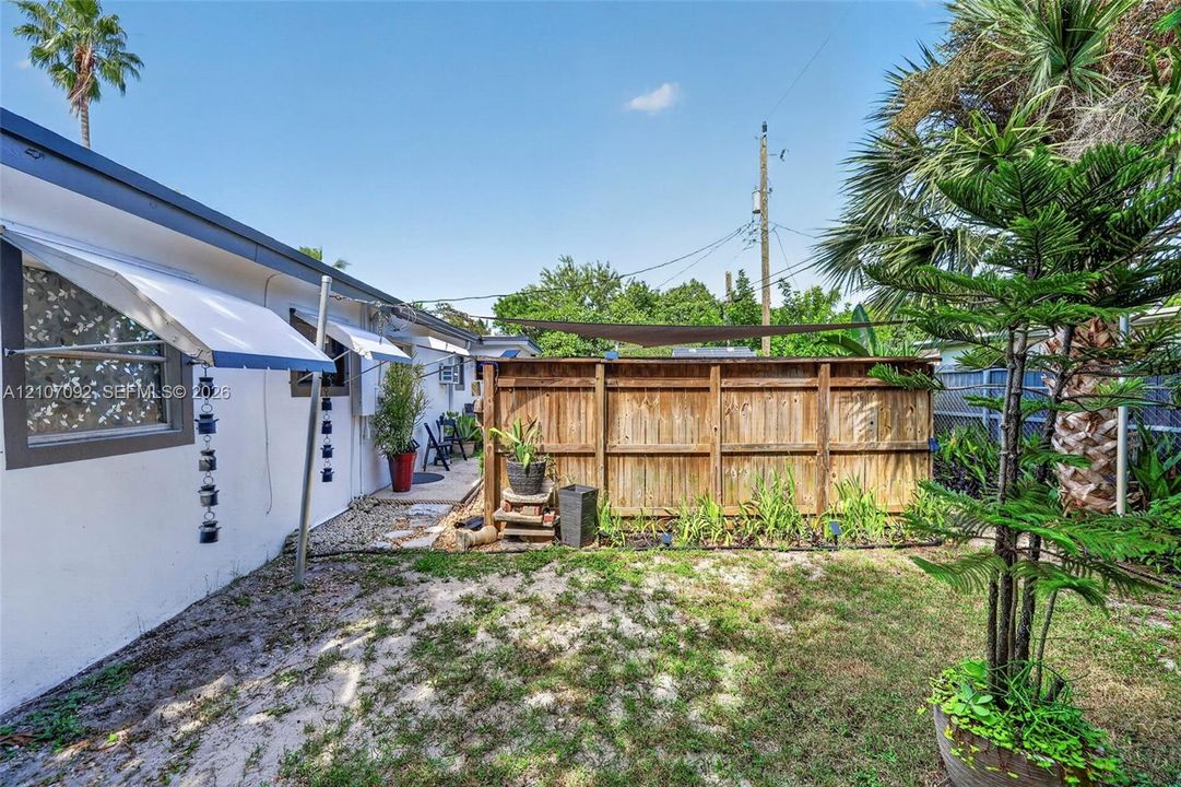 Private outdoor space featuring a wood perimeter fence, retractable sun shade, wall-mounted window awnings, and established landscaping