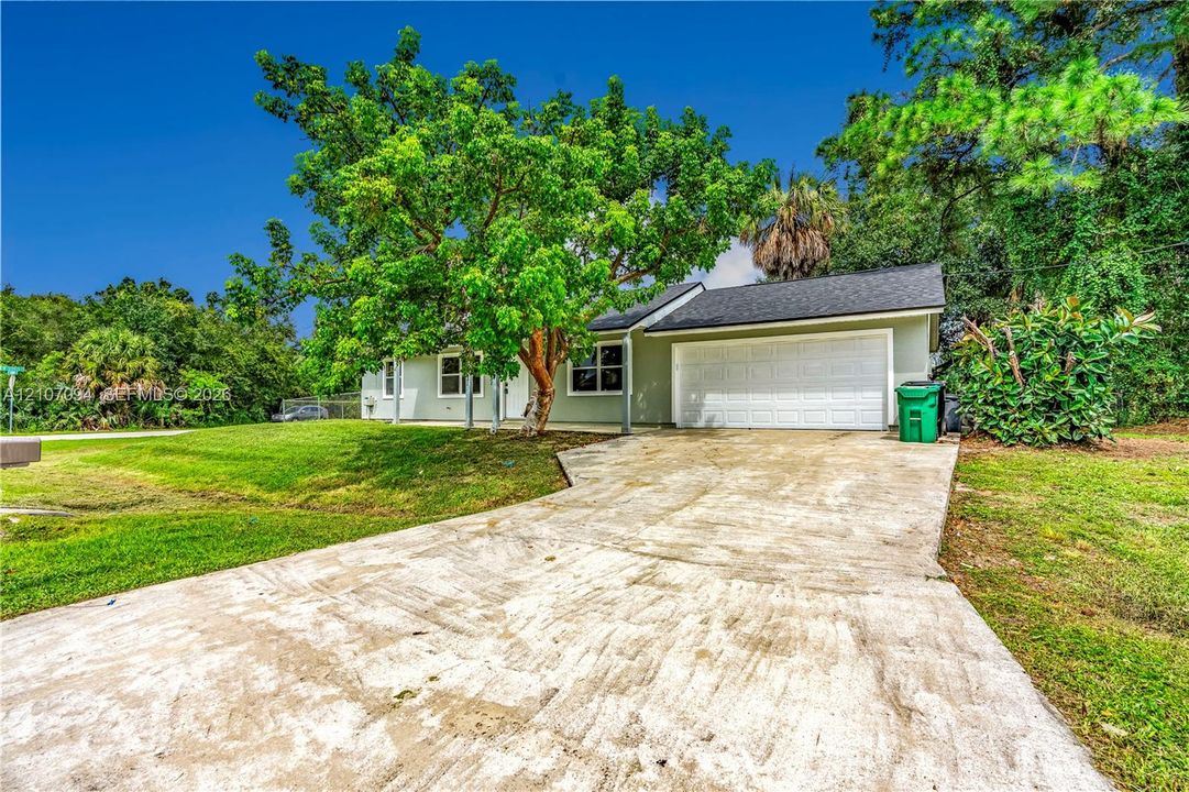 Single-story exterior featuring a concrete driveway, two-car garage, and mature trees on a landscaped lot