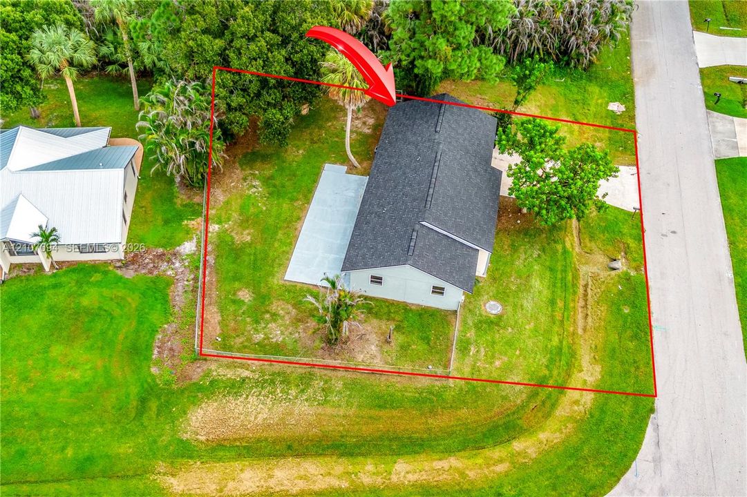 Aerial view of property featuring a detached residence with a composite shingle roof, concrete patio, concrete driveway, and mature landscaping on a grass-covered lot