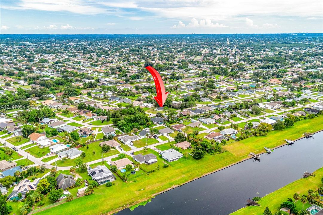 Aerial view of the residential property featuring mature trees, a multi-pitched roofline, and access to a canal