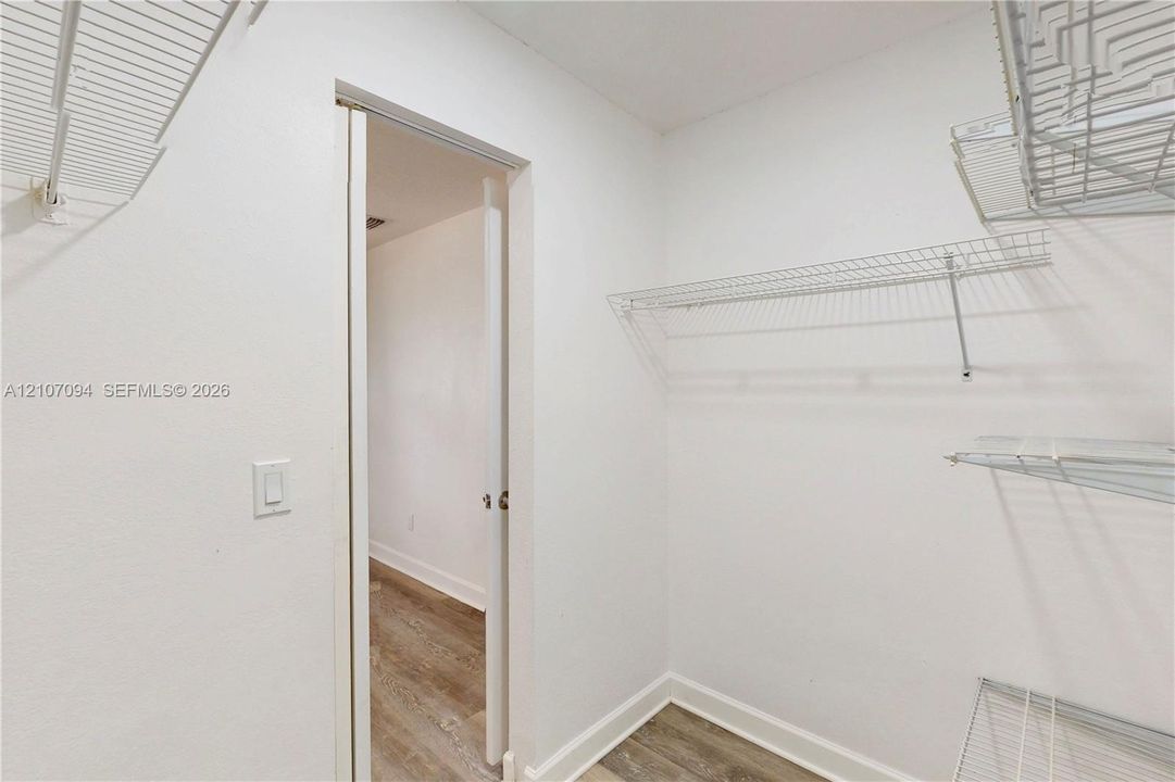 Storage area featuring white wall-mounted wire shelving and wood-finish flooring