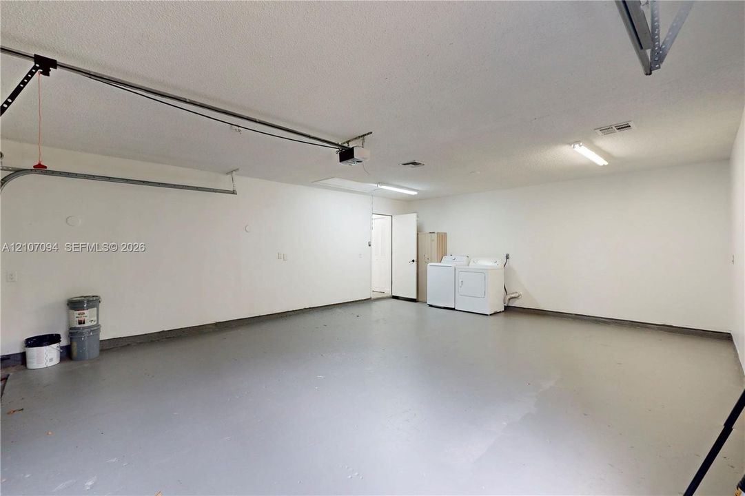 Two-car garage featuring a painted concrete floor, textured ceiling, fluorescent lighting, and dedicated laundry hookups
