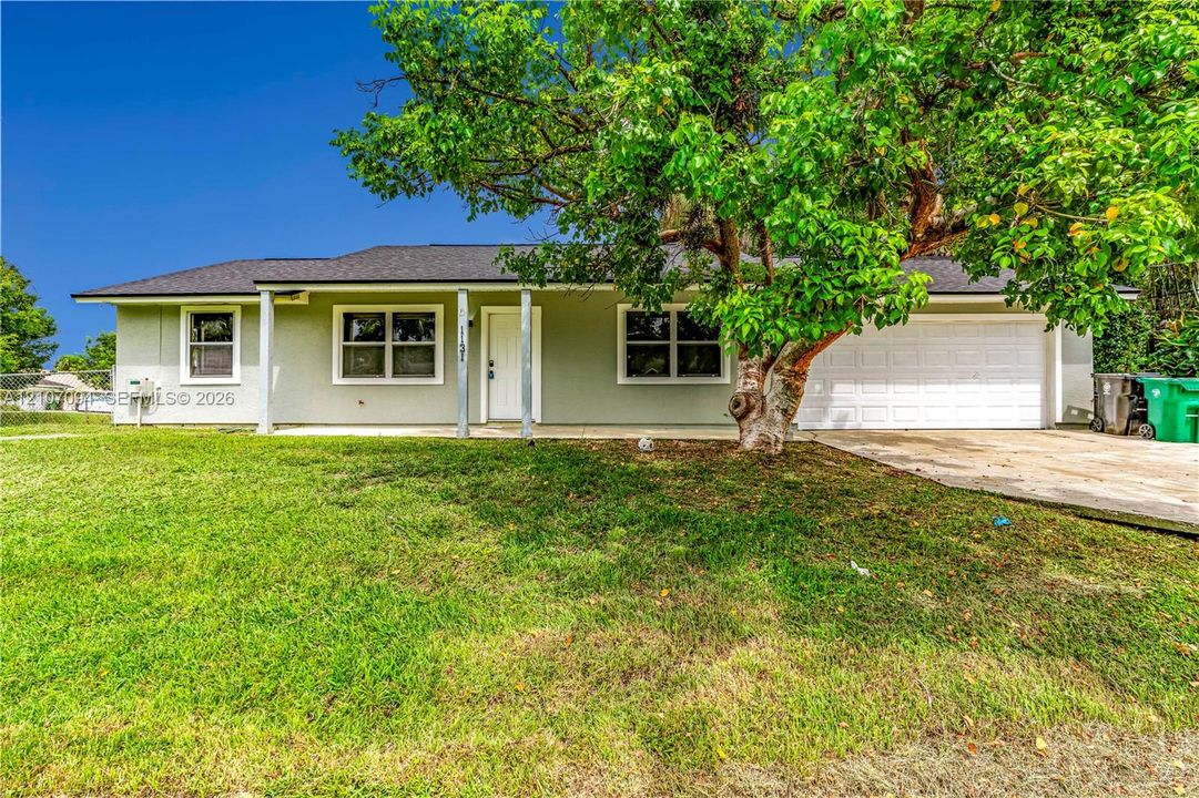 Single-story residence featuring a light-toned exterior, concrete driveway, attached garage, covered front porch, and expansive lawn