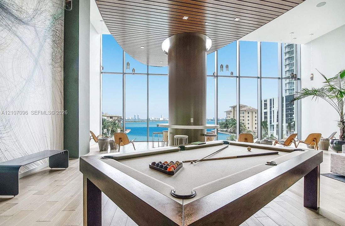 Floor-to-ceiling windows featuring panoramic water scenery, linear wood-slat ceiling detailing, hardwood flooring, and a central structural column with a built-in counter