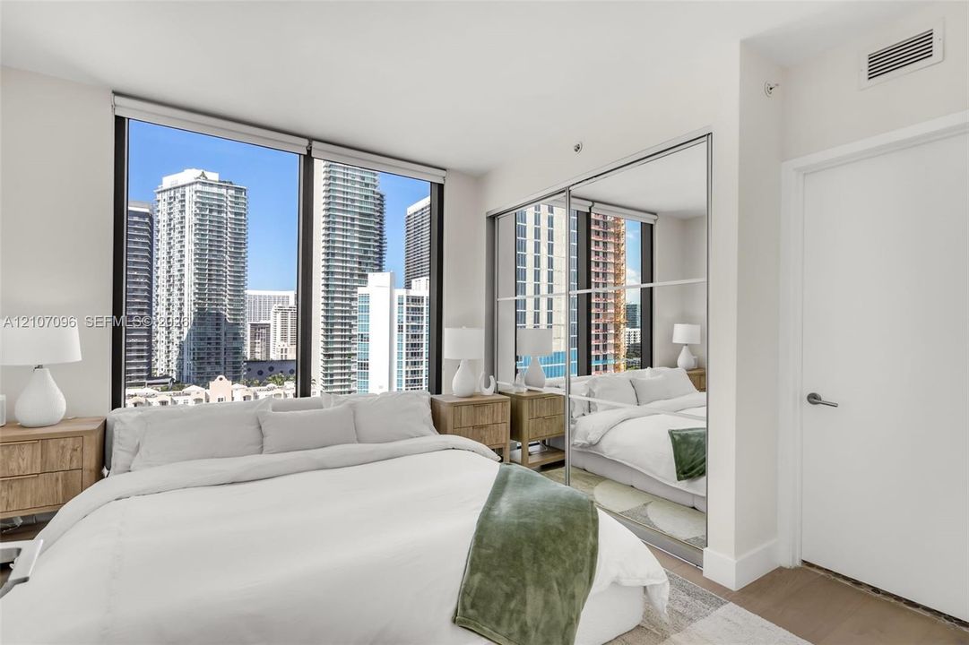 Floor-to-ceiling windows, mirrored sliding closet doors, and wood-finish flooring