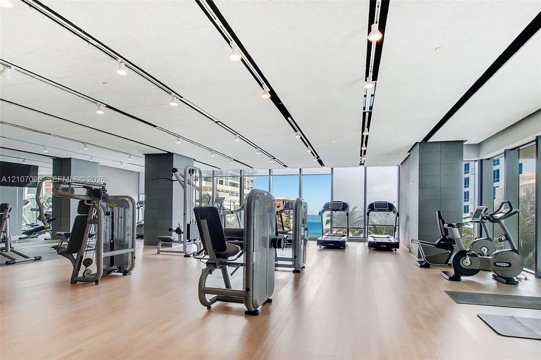Fitness center featuring floor-to-ceiling windows, wood-finish flooring, recessed track lighting, and tiled structural columns