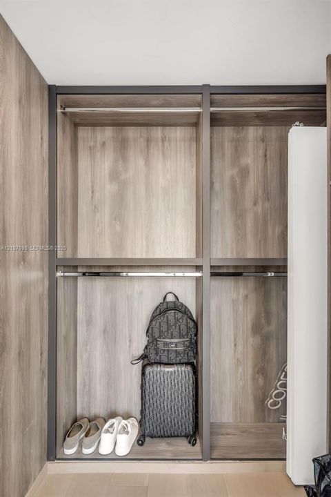 Built-in closet featuring wood-finish laminate cabinetry, metal frame detailing, and dual-level metal hanging rods