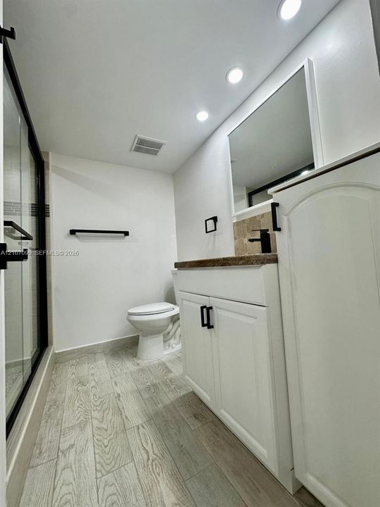 Bathroom featuring a vanity with stone-finish countertop, matte black hardware, recessed ceiling lighting, a walk-in shower with glass enclosure, and wood-finish flooring
