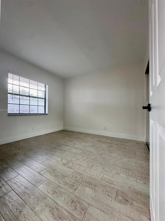 Room featuring wood-finish tile flooring, neutral wall paint, and a window with horizontal blinds