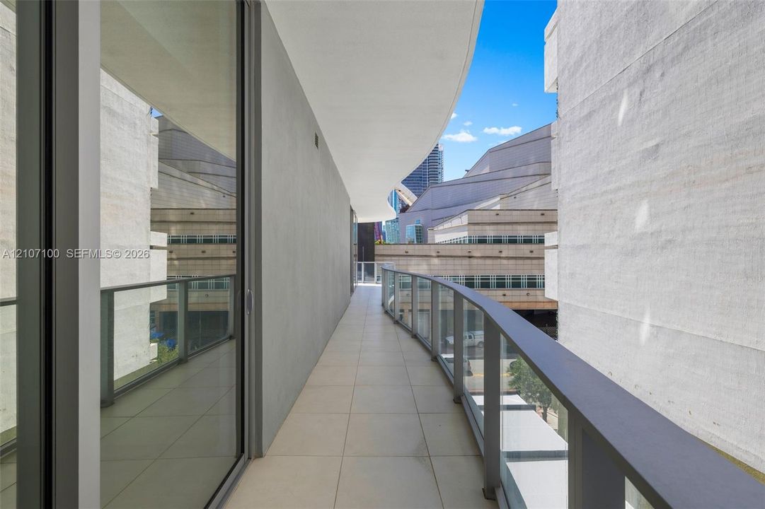 Covered balcony featuring large-format tile flooring and a glass railing with metal trim