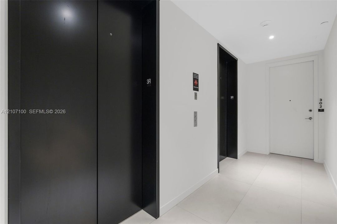 Elevator vestibule featuring large-format tile flooring, matte black elevator doors, and a solid-core entry door with brushed nickel hardware