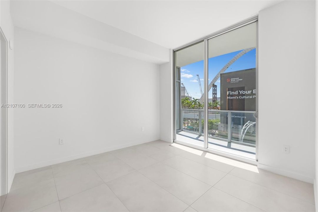 Floor-to-ceiling sliding glass doors, large format neutral floor tiling, and a private balcony featuring metal railing