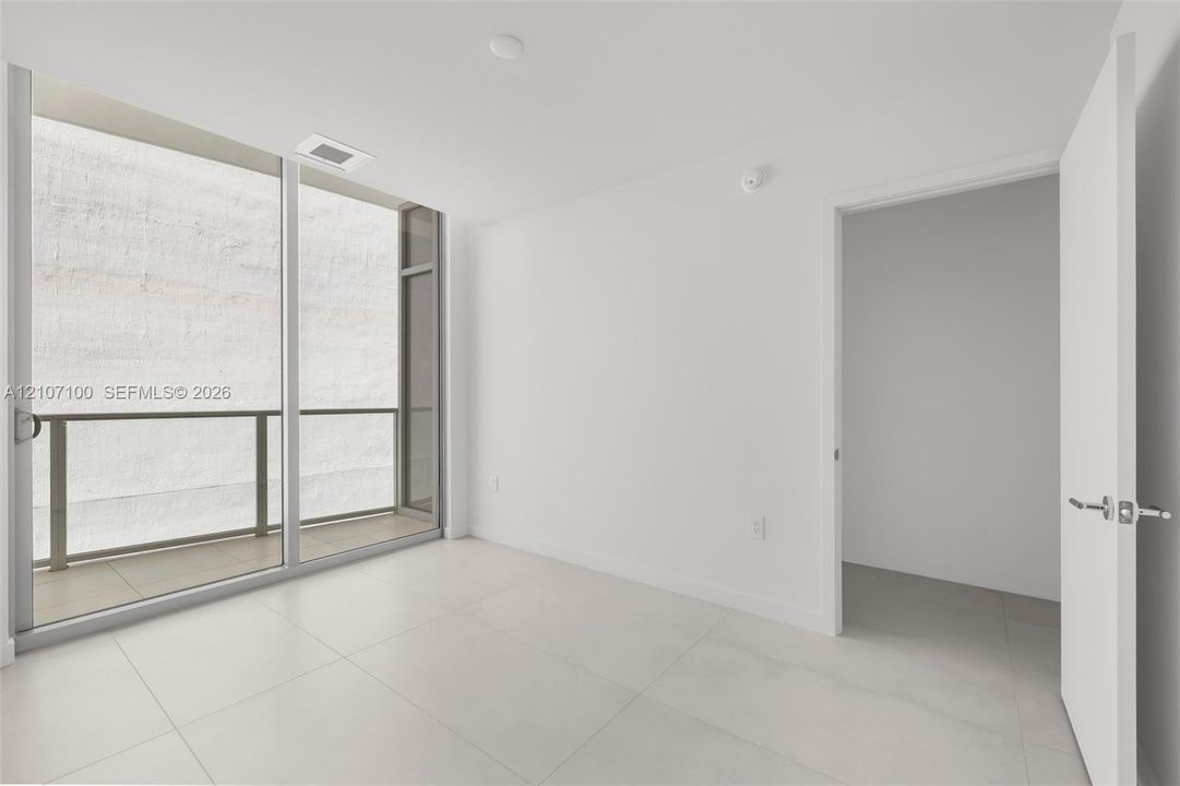 Large-format tile flooring, floor-to-ceiling glass sliding door, and private balcony with metal railing