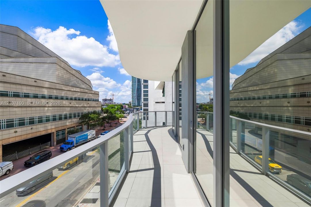 Curved balcony featuring tile flooring, full-height glass sliding doors, and a glass-paneled railing