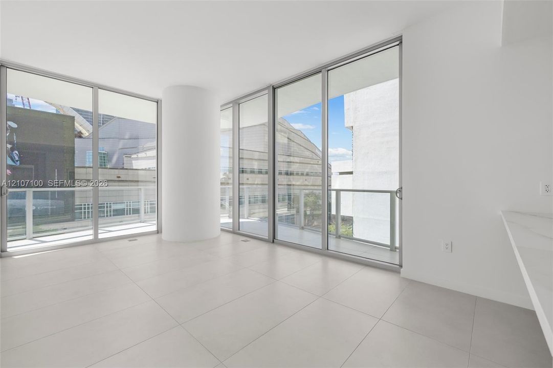 Floor-to-ceiling glass walls, expansive balcony access, neutral large-format tile flooring, and integrated white stone-finish countertop