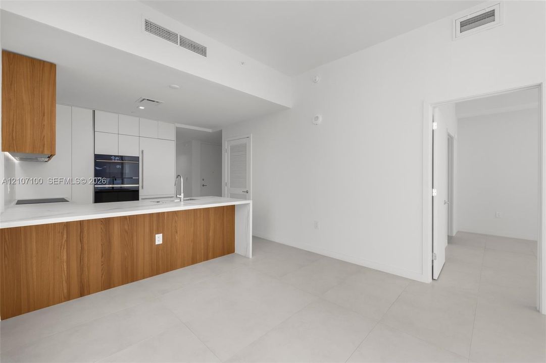 Kitchen featuring flat-panel wood-finish and white cabinetry, stone-finish countertops, integrated wall oven, and light-tone tile flooring