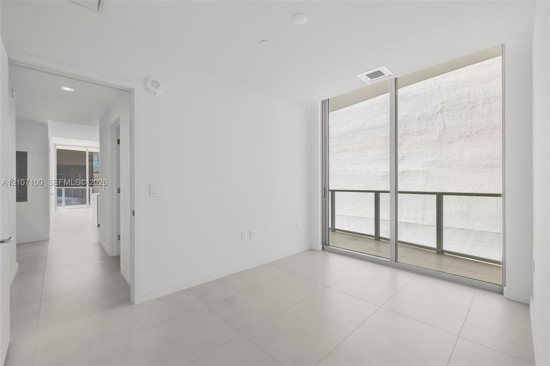 Floor-to-ceiling sliding glass door, private balcony with metal railing, and large-format tile flooring