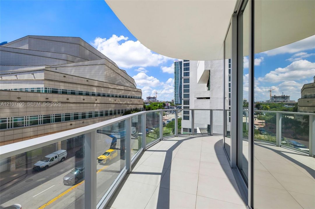 Private balcony featuring a curved structural design, glass panel railings, and large-format tile flooring