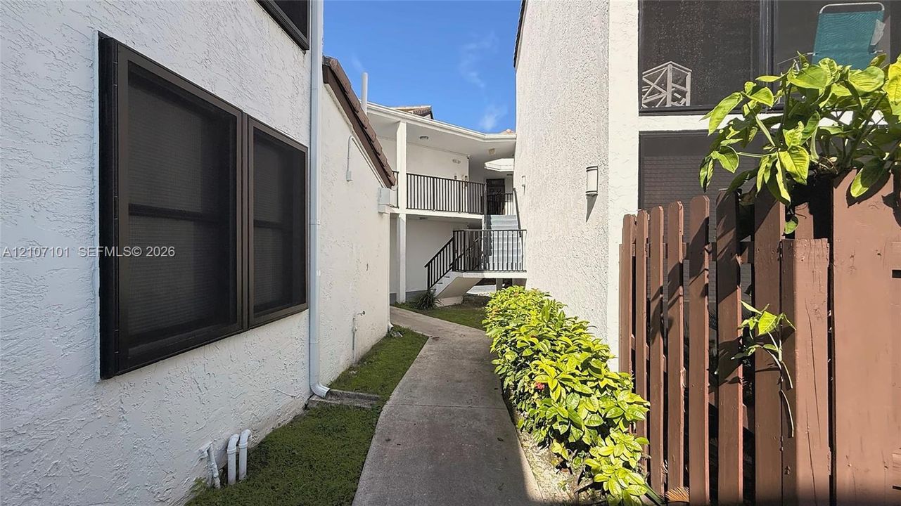 Stucco exterior featuring dark-framed windows, a concrete walkway, a wood-slat privacy fence, and a multi-level staircase with metal railings