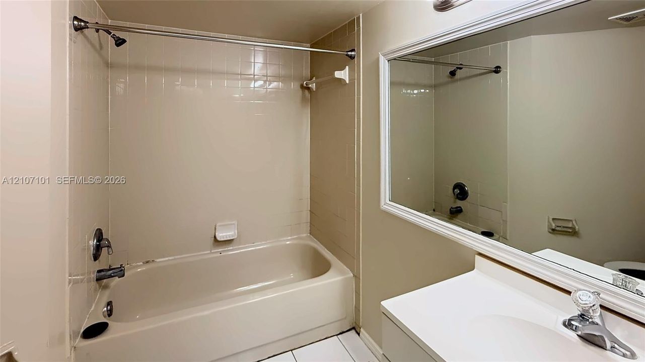 Bathroom featuring a white tub-shower combination with tiled surround, large vanity mirror with white frame, and white integrated sink basin