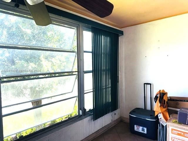 Multi-pane jalousie windows, ceiling-mounted paddle fan, and ceramic tile flooring