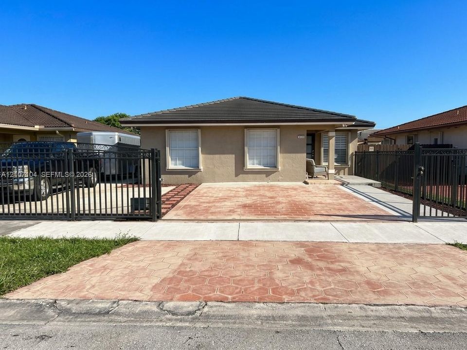 Single-story residence featuring a low-slope roof, stucco exterior, stamped concrete driveway, and a metal perimeter fence