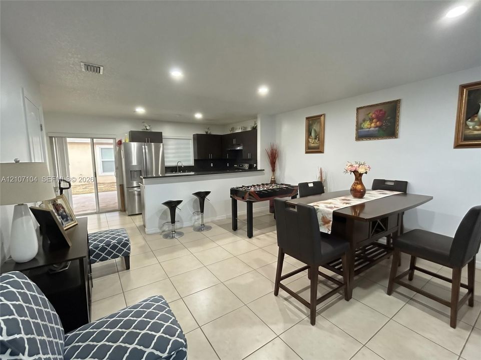 Open-concept area featuring ceramic tile flooring, recessed lighting, and a kitchen with dark cabinetry, stone-surface countertops, and a breakfast bar