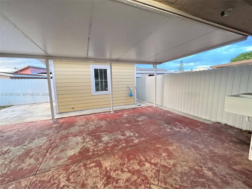 Covered outdoor patio featuring a concrete floor, horizontal siding, a multi-pane window, and a white privacy fence