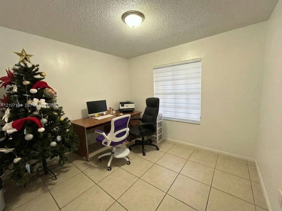 Neutral-toned room featuring large-format ceramic tile flooring, textured ceiling, flush-mount light fixture, and window with adjustable roller shade