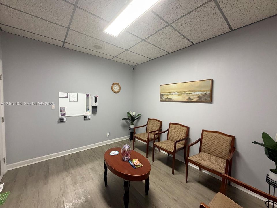 Neutral-toned interior space featuring wood-finish flooring, a suspended acoustic tile ceiling, and a built-in wall-mounted pass-through window