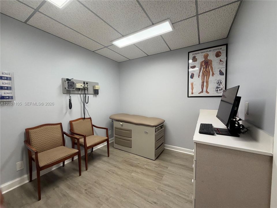 Room featuring wood-finish flooring, a drop ceiling with integrated rectangular lighting, and a wall-mounted utility console