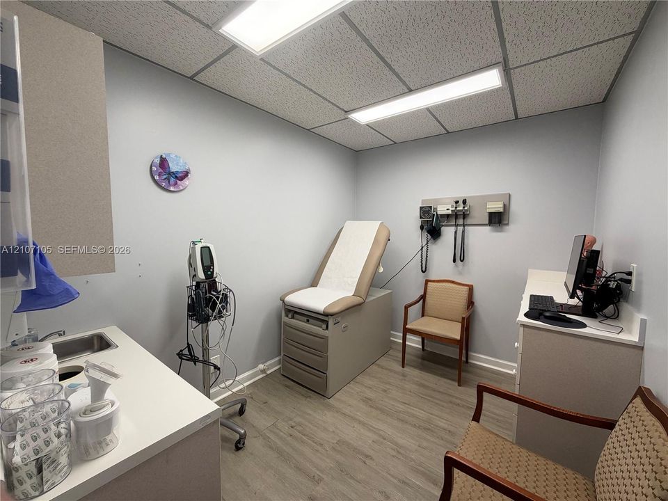 Room featuring wood-finish flooring, drop ceiling with recessed rectangular lighting, and built-in laminate cabinetry with a drop-in sink