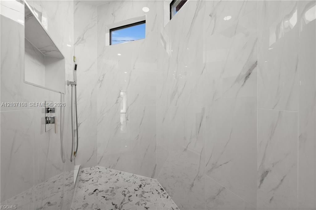 Walk-in shower featuring large-format stone-pattern wall tile, recessed built-in shelving, a handheld shower fixture, and clerestory windows