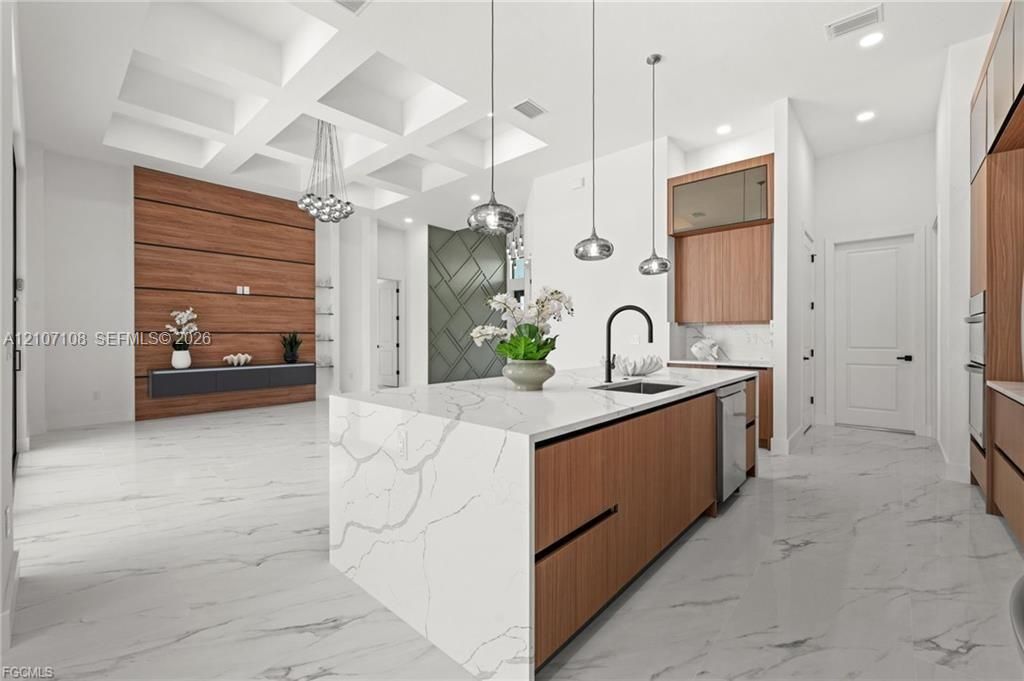 Kitchen featuring an expansive island with waterfall-edge stone countertop, wood-finish cabinetry, coffered ceiling, stone-finish flooring, and statement pendant lighting