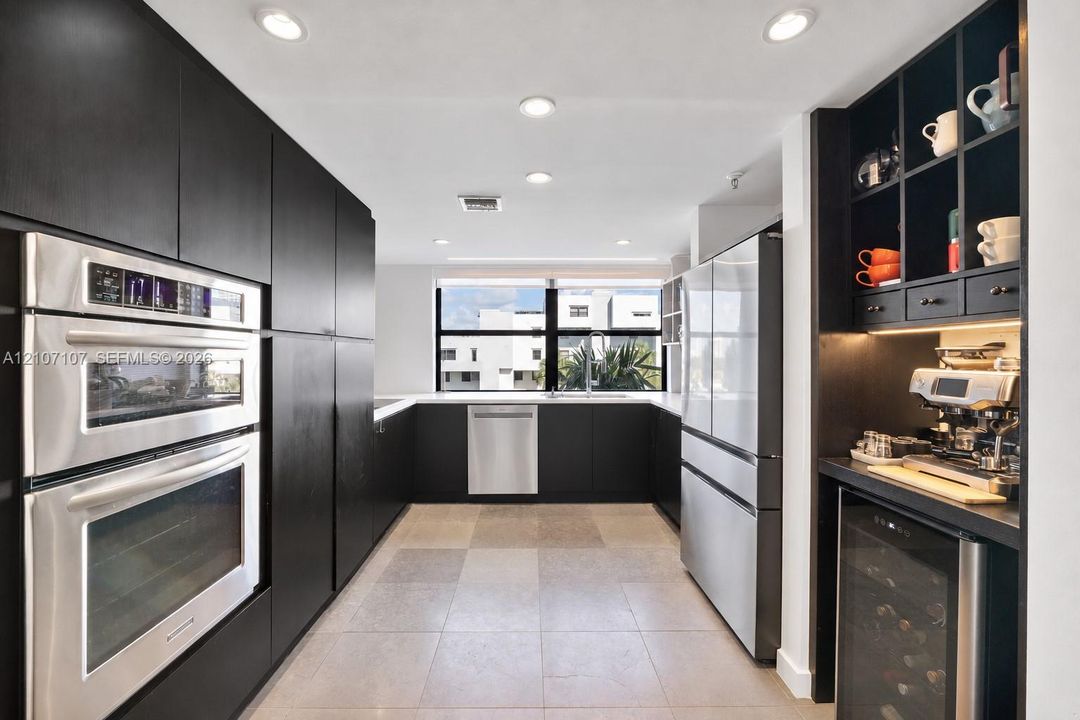 Kitchen featuring flat-panel dark cabinetry, built-in double wall ovens, integrated stainless steel appliances, under-cabinet lighting, and built-in beverage refrigerator