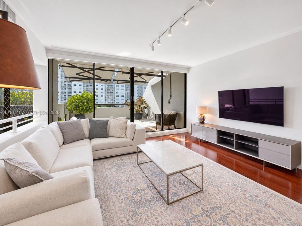 Living area featuring floor-to-ceiling glass sliding doors, wood-finish flooring, a wall-mounted media console, and adjustable multi-head track lighting