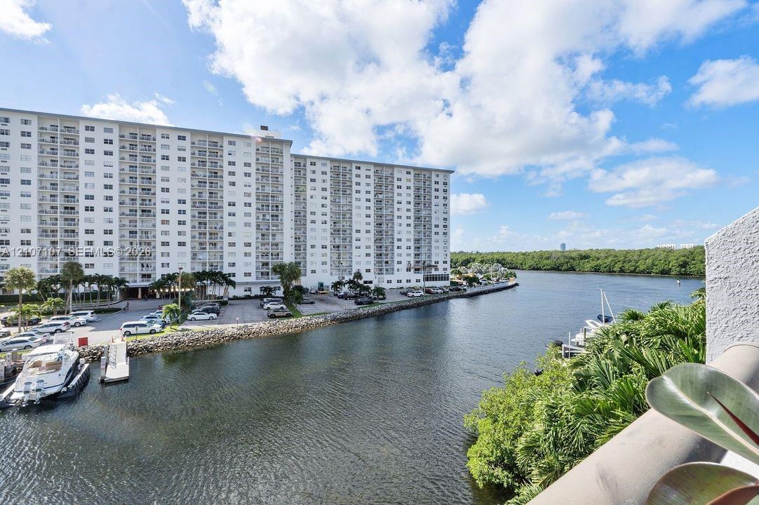 Waterfront balcony featuring a concrete railing, overlooking a canal, boat slips, mature landscaping, and multi-story high-rise architecture