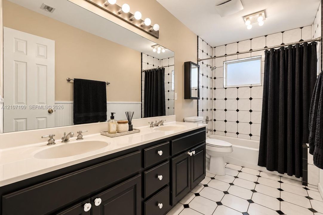 Dual-sink vanity with a solid-surface countertop, floor-to-ceiling tiled shower enclosure featuring inset accent tiles, expansive wall-mounted mirror, and decorative tile flooring