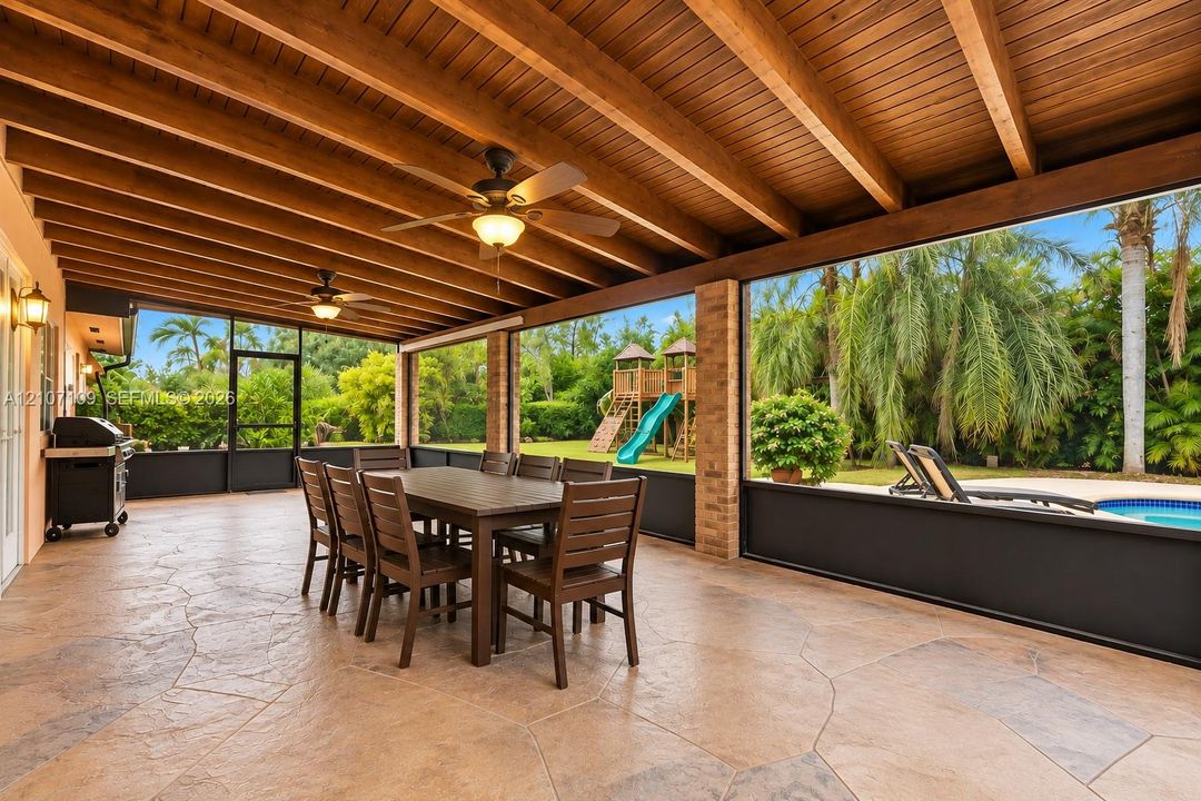 Covered patio featuring an exposed wood-beam ceiling, stamped concrete flooring, brick support columns, and full-height screen enclosure