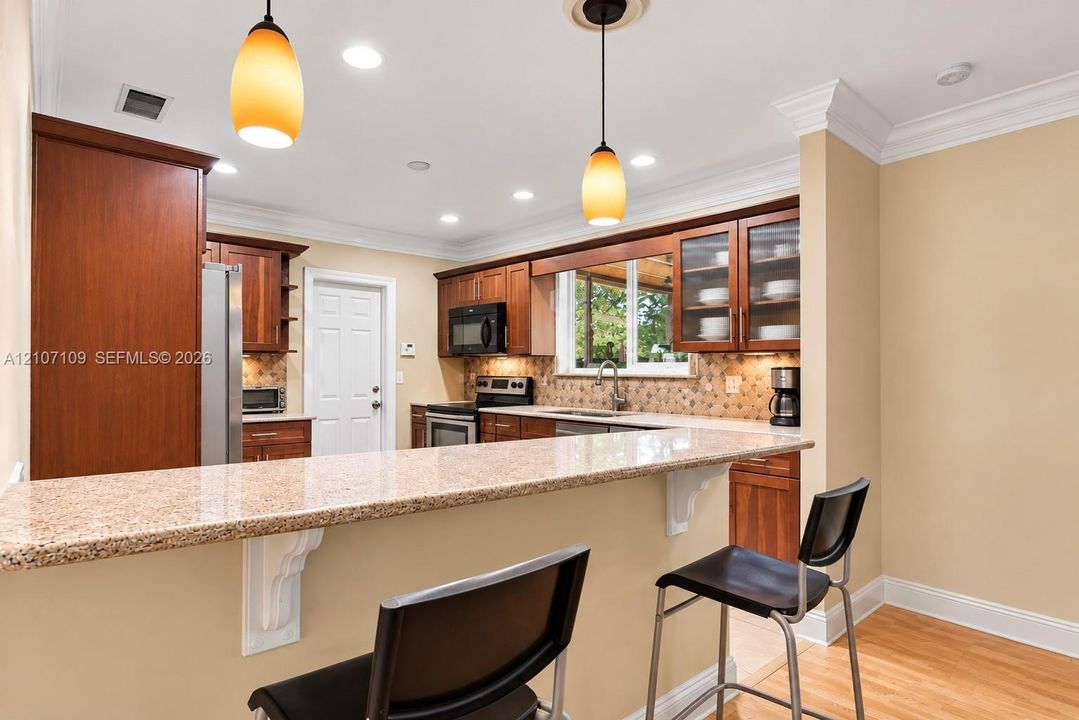 Kitchen featuring warm-tone wood cabinetry, stone-surfaced peninsula countertop, crown molding, recessed lighting, and pendant fixtures