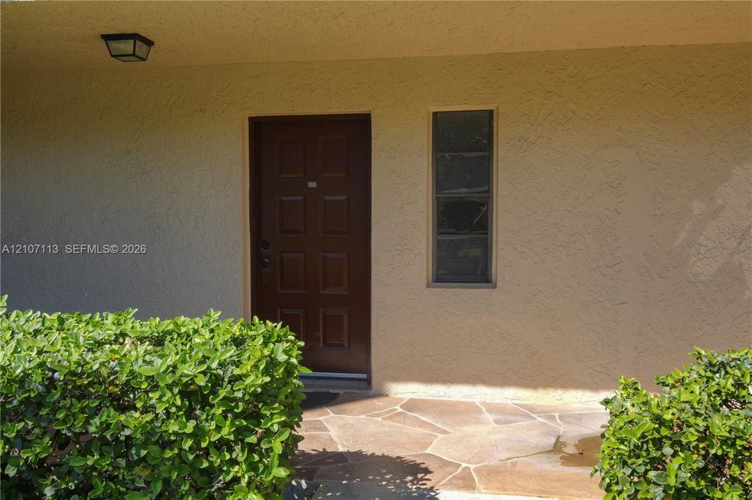 Entrance featuring a six-panel dark wood door, stucco exterior finish, flagstone paving, and flush-mount exterior lighting