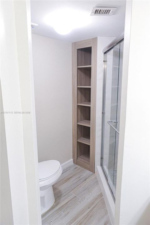 Built-in wood-finish shelving, walk-in shower with glass enclosure, and wood-finish flooring