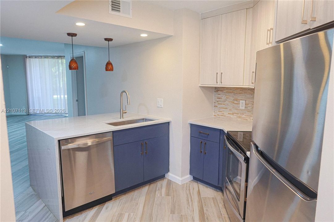 Kitchen featuring stainless steel appliances, dual-tone cabinetry, stone-style countertop, undermount sink with arched faucet, and stone-tiled backsplash