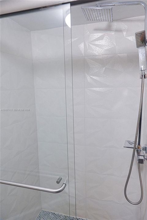 Walk-in shower featuring textured geometric wall tile, frameless glass door, rain-style showerhead, handheld sprayer, and mosaic tile flooring