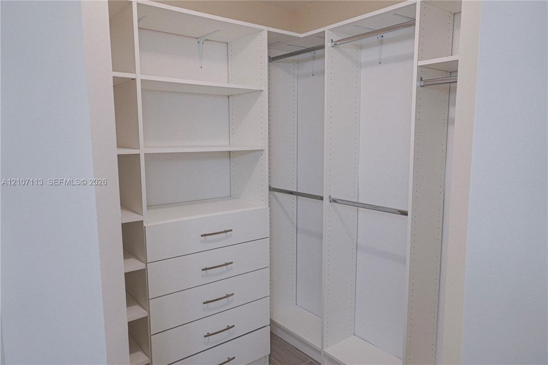 Built-in closet system featuring white modular cabinetry, adjustable shelving, integrated five-drawer dresser, and multiple stainless steel hanging rods