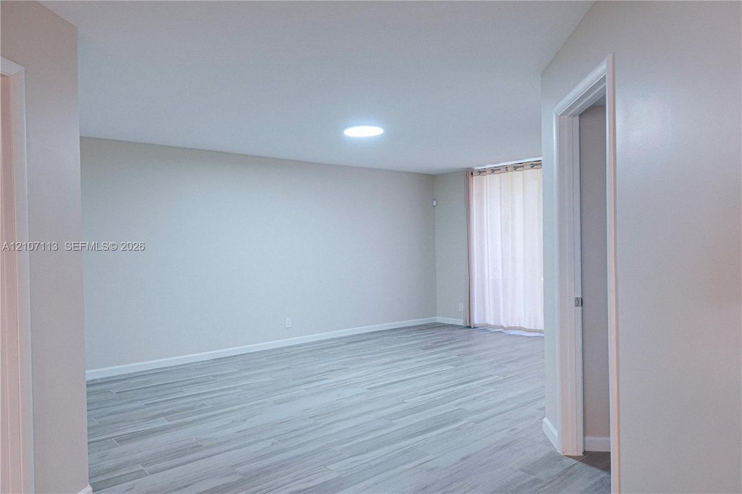 Neutral interior space featuring wood-finish flooring, a ceiling-mounted skylight, and a sliding glass door