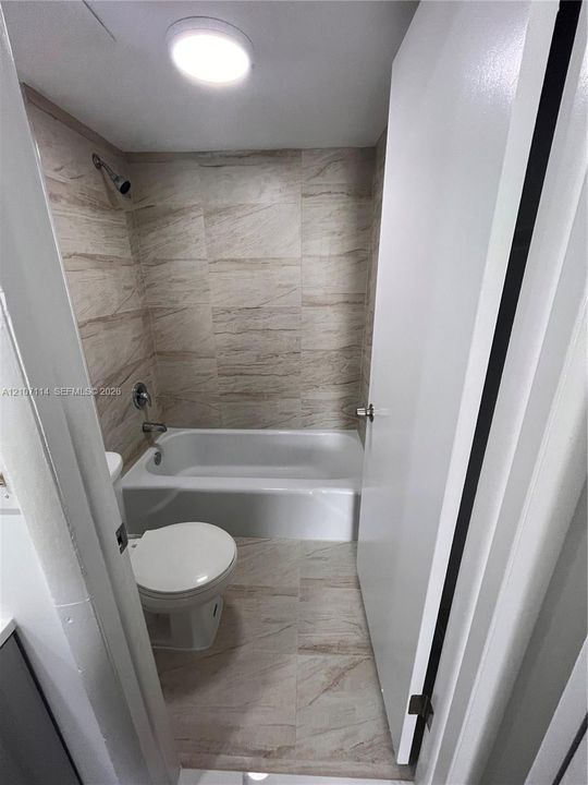 Bathroom featuring floor-to-ceiling tile surround, recessed lighting, and a white soaking tub
