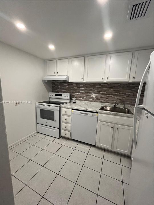 Kitchen featuring white cabinetry, stone-finish countertops, tile backsplash, built-in dishwasher, and large-format floor tiling