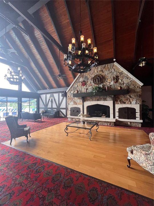 Vaulted ceiling with exposed wood beams, stone fireplace with a substantial mantel, wood-finish flooring, and ornate chandeliers